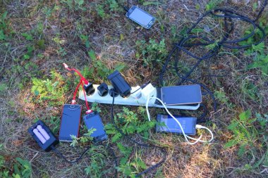 Birçok pil, akıllı telefonlar için şarj aletleri ve elektrikli uzatma kabloları, ekran şarj oluyor, çimenlerin üzerinde uzanır