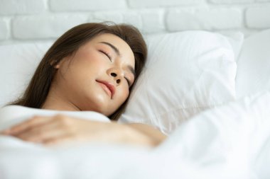 Yatak odasındaki beyaz yatakta uyuyan güzel bir kadın, tatlı rüyalar, gözlerini kapalı tutuyor, evde güzel bir dinlenme ve sakin bir ortam sağlıyor. İnsanlar ve dinlenme kavramı.