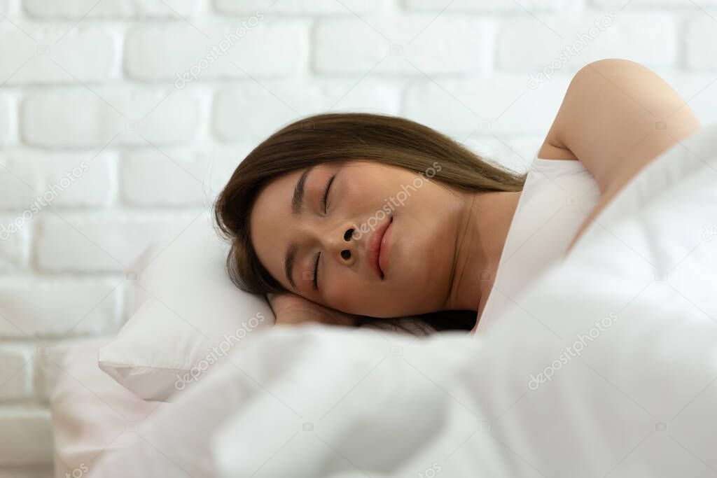 Beautiful woman sleeping on white bed in the bedroom,sweet dreams, keeps eyes closed, enjoys good rest at home and calm atmosphere. People and rest concept.