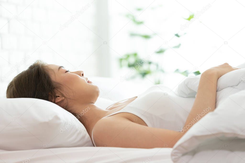 Beautiful woman sleeping on white bed in the bedroom,sweet dreams, keeps eyes closed, enjoys good rest at home and calm atmosphere. People and rest concept.