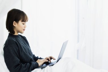 Evde dizüstü bilgisayarda çalışan güzel Asyalı kadın. Sosyal uygulamaları ve çalışmaları kontrol eden kadın. Ev konseptinden çalışma..