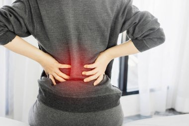 Asyalı bir kadın sırt ağrısı çekiyor ve sabahları yatakta oturuyor. Renkli bir ton.