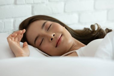 Yatak odasındaki beyaz yatakta uyuyan güzel bir kadın, tatlı rüyalar, gözlerini kapalı tutuyor, evde güzel bir dinlenme ve sakin bir ortam sağlıyor. İnsanlar ve dinlenme kavramı.