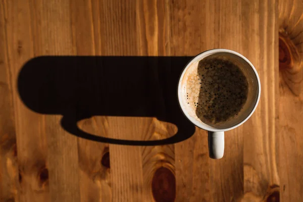 Yüksek açılı kahve fincanı, tahta bir masada gölgesi var.