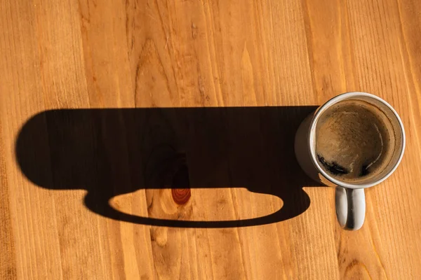 Yüksek açılı kahve fincanı, tahta bir masada gölgesi var.