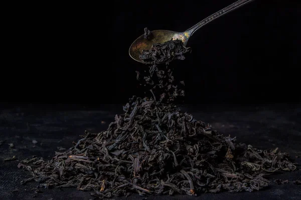 Stock image Tea leaves pouring from a teaspoon on a black background