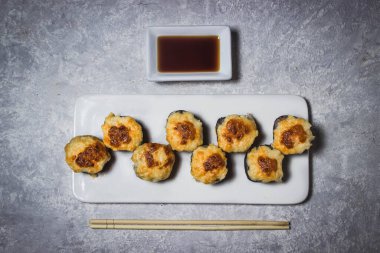 Beyaz bir tabakta yuvarlanıyor. Yanında Çin çubukları ve soya sosu var. Beyaz arkaplanda fotoğraf