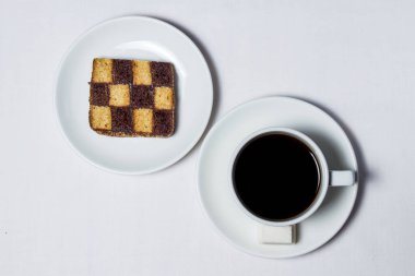 Satranç pişirme ve beyaz masa örtüsünün üzerinde bir fincan kahve. Çay takımı da beyaz.