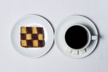 Satranç pişirme ve beyaz masa örtüsünün üzerinde bir fincan kahve. Çay takımı da beyaz.