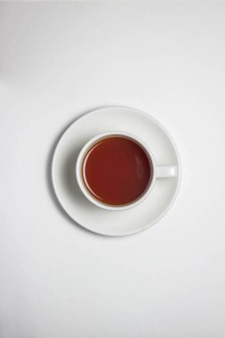 Beyaz bardakta bir fincan çay ve beyaz masa örtüsünün üstünde bir fincan çay. Fotoğrafın ortasında bir fincan çay var..