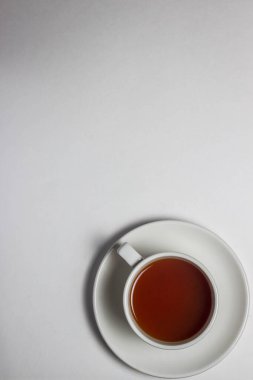 Beyaz bardakta bir fincan çay ve beyaz masa örtüsünün üstünde bir fincan çay. Fotoğrafın sağ alt tarafında bir fincan çay var..