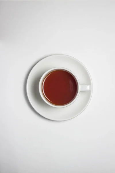 Beyaz bardakta bir fincan çay ve beyaz masa örtüsünün üstünde bir fincan çay. Fotoğrafın ortasında bir fincan çay var..