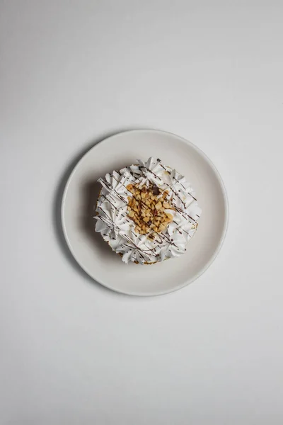 Cake with white cream and nut crumbs on a white saucer. The cake is located in the middle of the photo