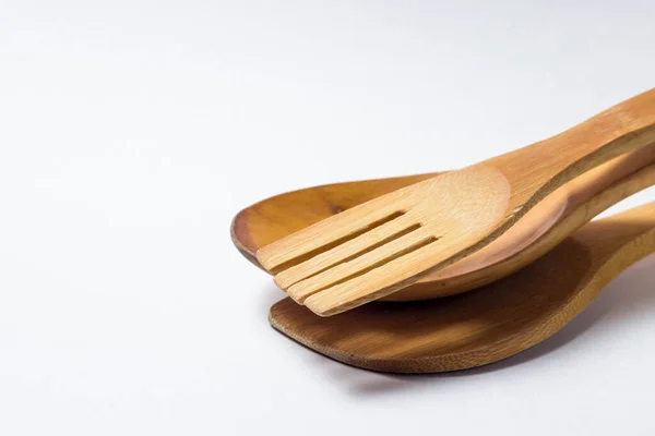 Three wooden cutlery lie on each other on the right side of the photo on a white background. Wooden spoon, wooden fork. Wooden spatula