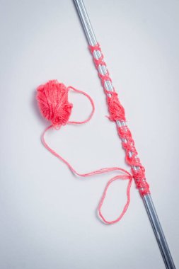 Kırmızı örgü ipliğine sarılı örgü iğneleri. Yakınlarda bir kırmızı örgü yumağı uzanıyor. Beyaz arkaplanda fotoğraf
