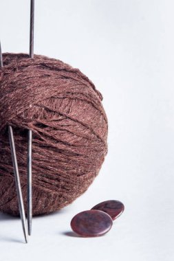 Bir top kahverengi iplik ve iki örgü iğnesi. Yakınlarda iki kahverengi düğme var. Beyaz arkaplanda fotoğraf