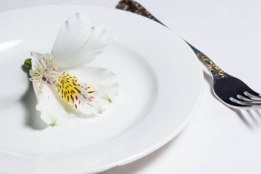 Beyaz bir tabakta beyaz bir çiçek. Yakınlarda bir çatal var.