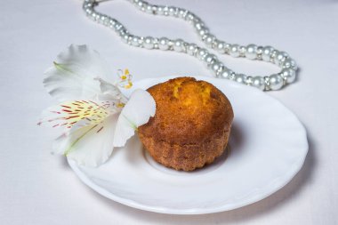 Kek ve beyaz bir tabakta beyaz çiçek. Yakınlarda beyaz inci mücevherler var.