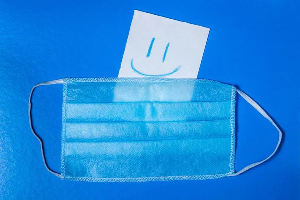 코로나 바이러스 의료용 마스크 파란색 배경에 미소가 그려진 종이가 있습니다 — 스톡 사진