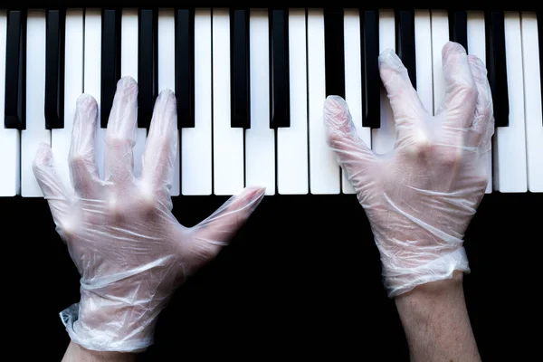 hands in medical gloves play the piano. black piano. white and black keys