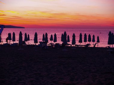 Gece deniz manzarası. İskele fenerlerle aydınlatılıyor. Plaj şemsiyesi ve güneşlik siluetleri..