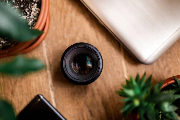 Düz yat. Laptop, cep telefonu, lens, ahşap bir arka planda çiçek standı. en üstteki görünüm