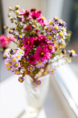Yumuşak odaklanma. Pencerede bir buket parlak kır çiçeği duruyor. Parlak güneş pencereden parlıyor. Parlak renkli kurutulmuş çiçek buketi.