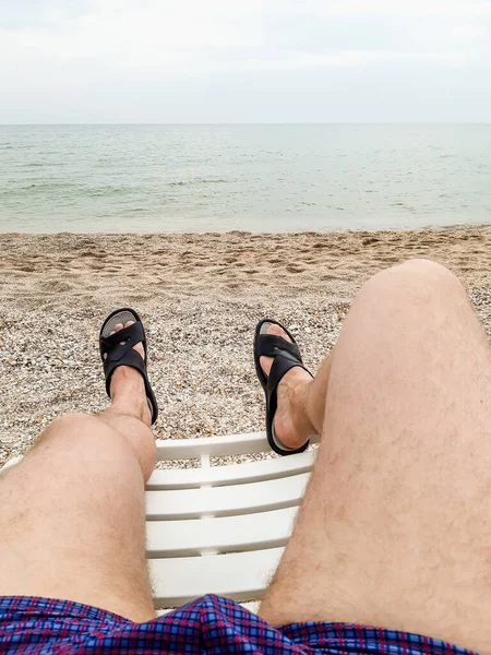man resting on the beach on a deck chair. male feet in slates on a deck chair.