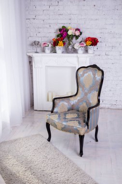 Beyaz bir odada gri katlanır koltuk. Şöminenin üzerinde parlak çiçekler.