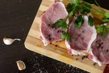 Yeşiller, baharatlar ve et kesme tahtasında. Üç biftek domuz eti, biber, sarımsak, tuz. Evde yemek pişir. taze yiyecek