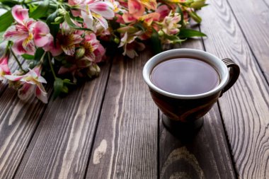 Bir fincan çay ve ahşap arka planda Alstroemeria. Kahverengi arka planda çiçekler. Metni kopyala Güzel buket..