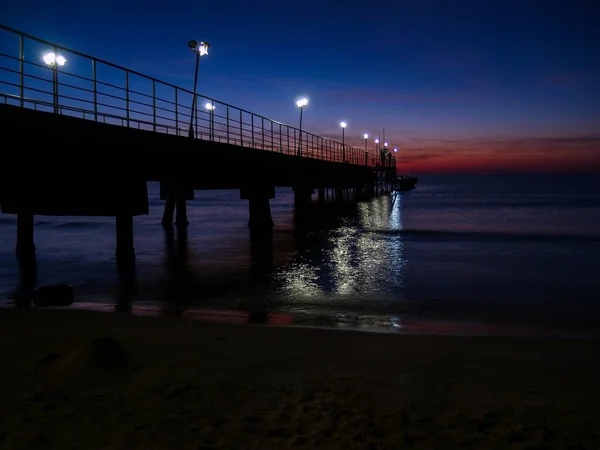 Nocny Pejzaż Morski Pomost Jest Oświetlony Latarniami Sylwetki Parasoli Plażowych — Zdjęcie stockowe