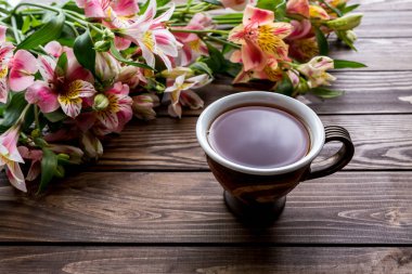 Bir fincan çay ve ahşap arka planda Alstroemeria. Kahverengi arka planda çiçekler. Metni kopyala Güzel buket..