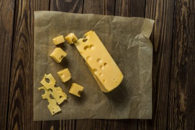 Maasdamer peyniri. Eski siyah ahşap bir masanın üzerinde ambalaj kağıdında dilimlenmiş peynir. Şarap ve romantizm için yemek, peynir lezzetleri. Menü tasarımı.