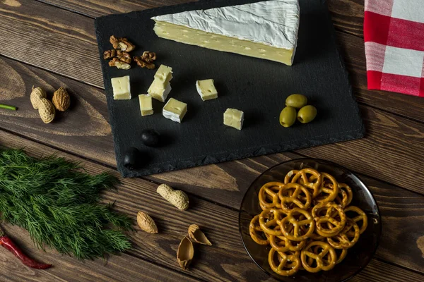 Camembert cheese. cheese dish with olives, herbs, snacks on an old black wooden table. brie cheese. Food for wine and romance, cheese delicacies. Menu design. napkin with a scottish pattern