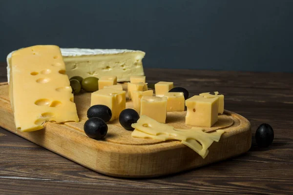 Tasting a cheese dish with olives on an old black wooden table. Food for wine and romance, cheese delicacies. Menu design horizontal. View from above.