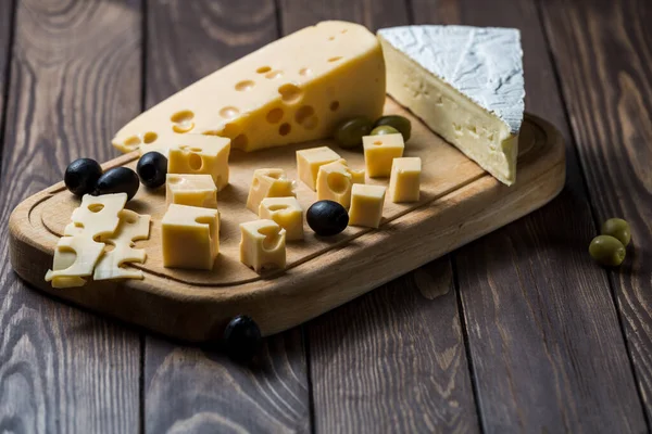 Tasting a cheese dish with olives on an old black wooden table. Food for wine and romance, cheese delicacies. Menu design horizontal. View from above.