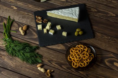 Camembert peyniri. Zeytinli peynir tabağı, otlar, eski siyah ahşap bir masada atıştırmalıklar. Brie peyniri. Şarap ve romantizm için yemek, peynir lezzetleri..