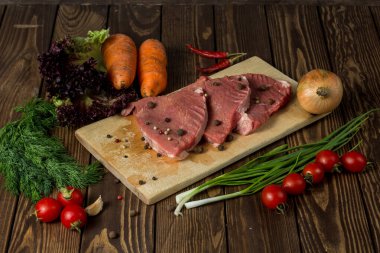 Kesme tahtasındaki çiğ et. Otlu biftek, vişneli domates, soğan, havuç ve dereotlu. Restoranın menüsü.