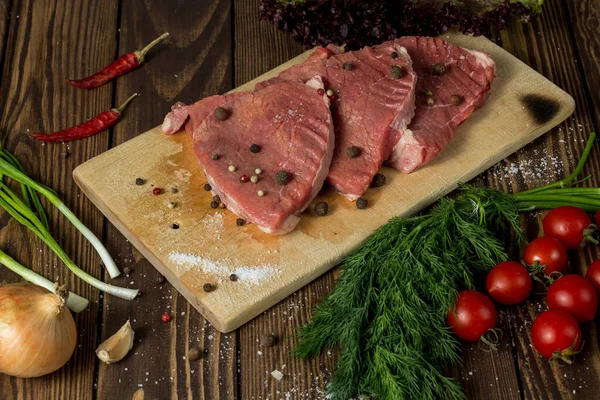 Taze organik sebzeler, soğan, sarımsak, baharatlar, biberiye, deniz tuzu, kiraz domatesleri ve baharatlarla ahşap kesilmiş et dilimleri. Restoranın menüsü.