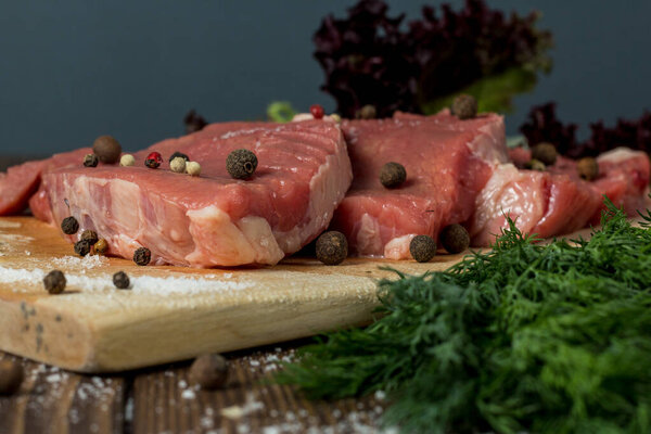 Raw meat beef slices on a wooden chopping board with fresh organic vegetables, onion, garlic, spices, peppercorn, rosemary, sea salt, cherry tomatoes and spices. menu for the restaurant.