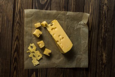 Maasdamer peyniri. Eski siyah ahşap bir masanın üzerinde ambalaj kağıdında dilimlenmiş peynir. Şarap ve romantizm için yemek, peynir lezzetleri. Menü tasarımı.