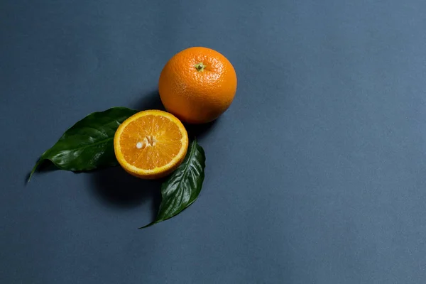 a whole orange and half an orange, and two green leaves are on a gray background.