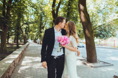 Gelin ve damat gün açık havada yürüyüş düğününde Doğa bahar. Gelin çift, mutlu yeni evli kadın adam yeşil park kucaklayan. Açık sevgi dolu.