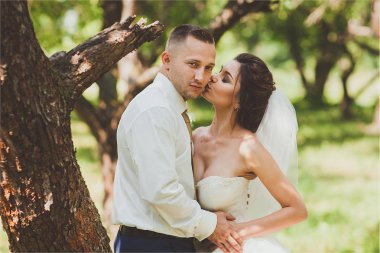 Gelin ve damat bir park kissing.couple yeni evliler doğa yeşil orman düğünde fotoğraf portre vardır.
