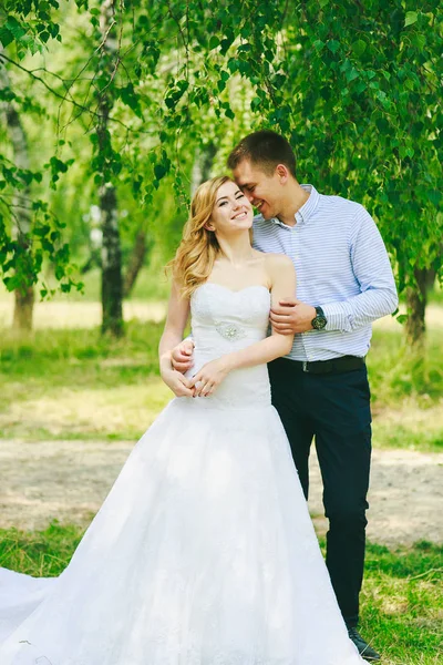 Gewoon liefdevolle hipster echtpaar in trouwjurk en pak op groene weide in een bos bij zonsondergang. gelukkige bruid en bruidegom lopen lopen en dansen in de zomer weide. Romantische getrouwd jong gezin — Stockfoto