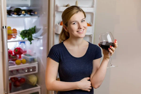 Jonge vrouw in het drinken van rode wijn in de buurt van de koelkast nachtkleding — Stockfoto