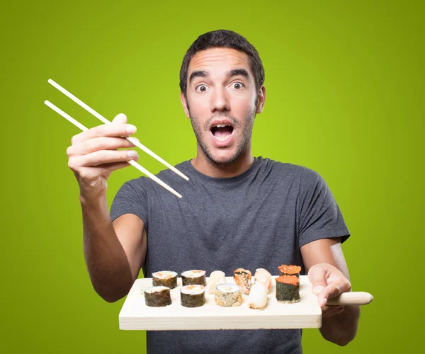 Surprised young man eating sushi on green background