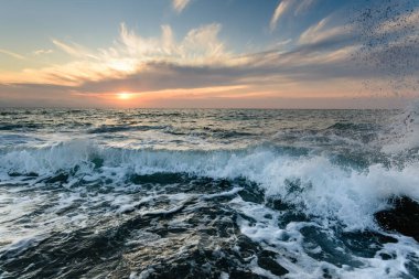 Okyanus ufkunda güneş batarken bir dalga kıyı şeridine doğru yuvarlanıyor..