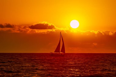 Okyanus boyunca yelken açan bir yelkenli Güneş Ufuktaki Bulutların üzerinde batarken